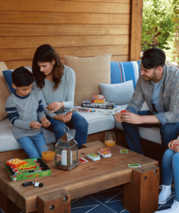 a family seated outside on a deck playing a card game 